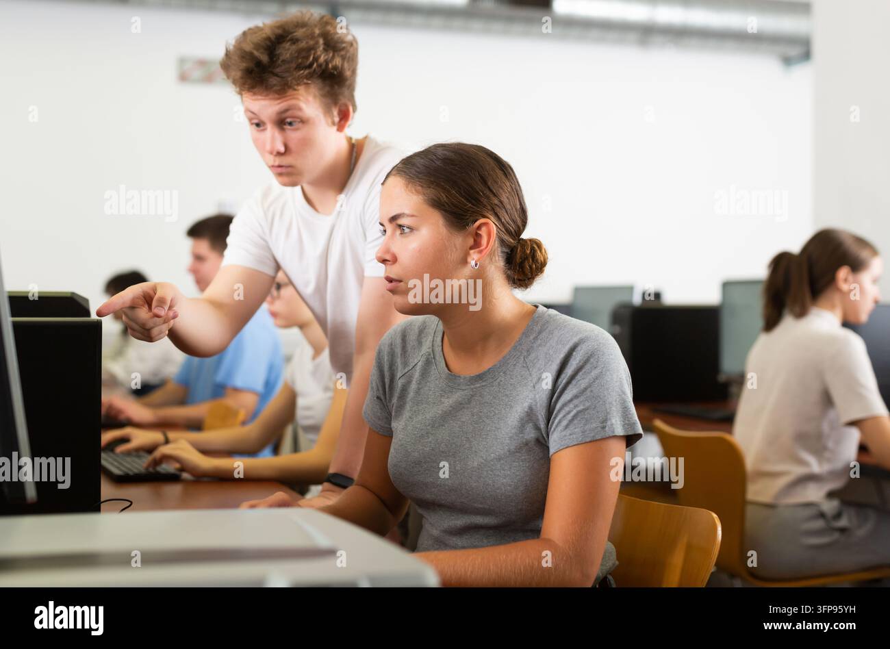 Schoolboy using computer and teacher helping to him in classroom Stock Photo