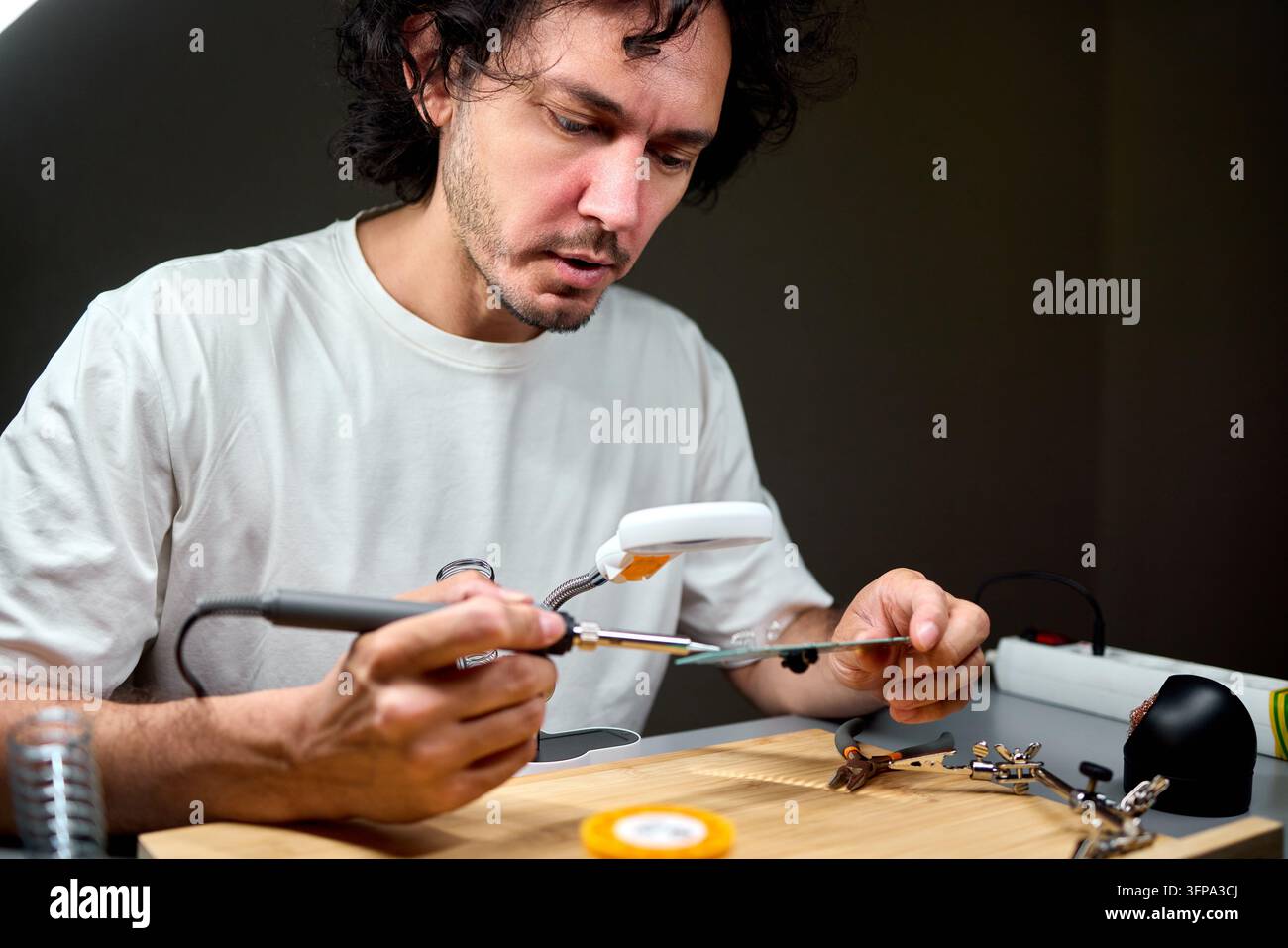 Man soldering electronic circuit on workbench under focused light Stock Photo