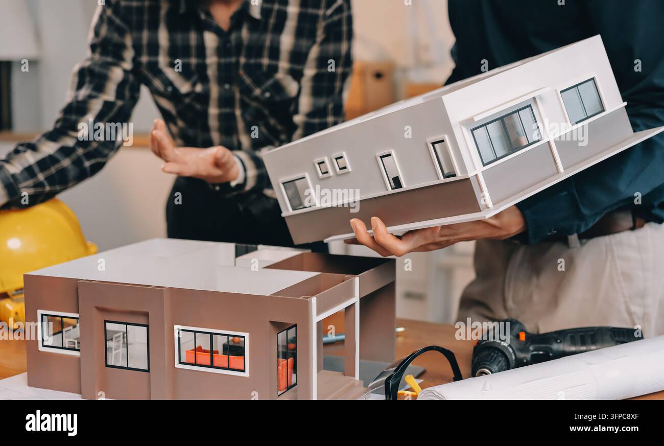 Asian architect and engineer team checking architectural house model using measuring tape on the table at office studio. Stock Photo
