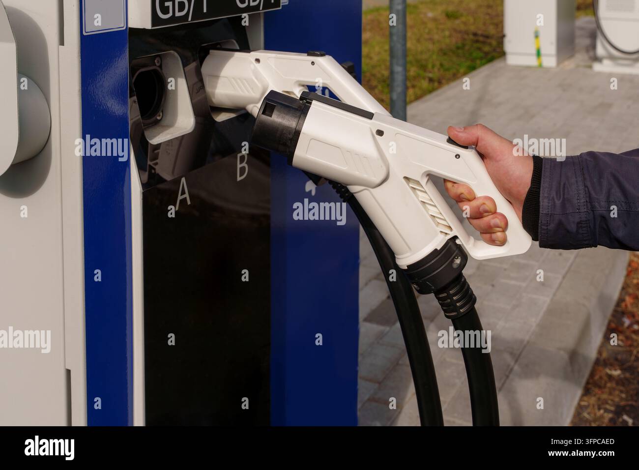 Man hand holding white GBT charging plug at public station. Interaction ...