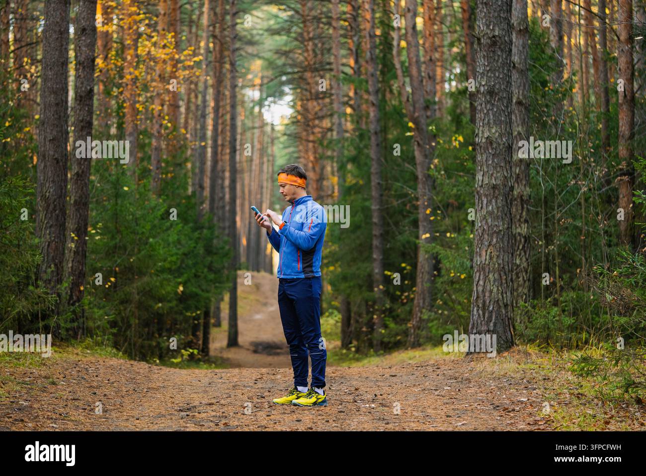 Man standing on a dirt trail in a tall pine forest while looking at his ...