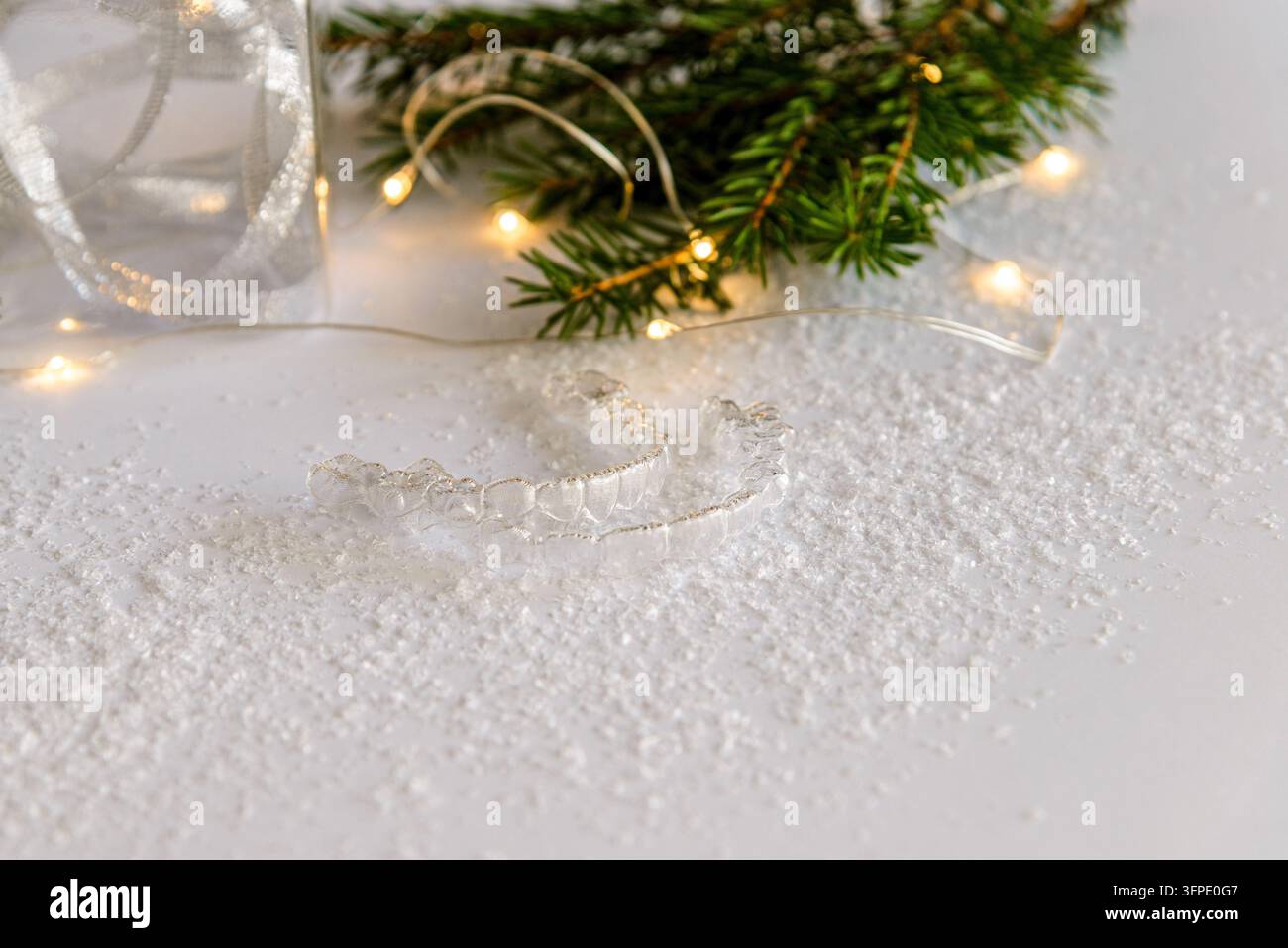 Clear Retyainers Clear dental aligners resting on artificial snow with fir branches and ...