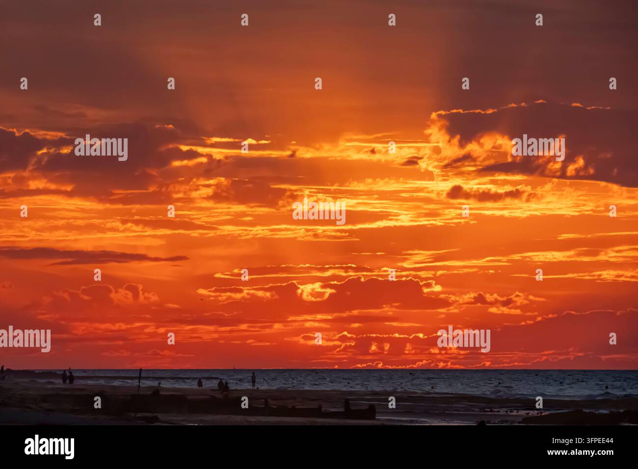 Sunset over the waves on the sea and the jetty from the beach with ...