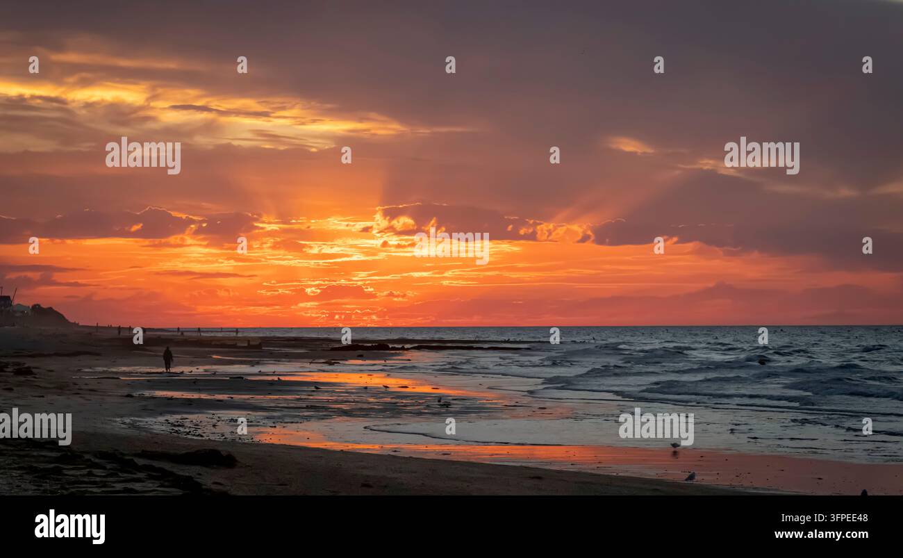 Sunset over the waves on the sea and the jetty from the beach with ...