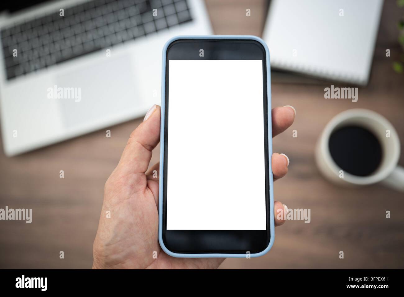 Hand holding smartphone with white blank screen above outdoor workspace ...