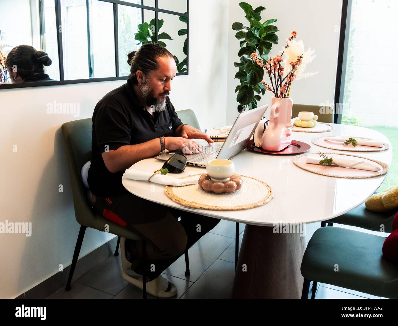 Comp Tabel Man working remotely on a laptop while seated at a dining table in a ...