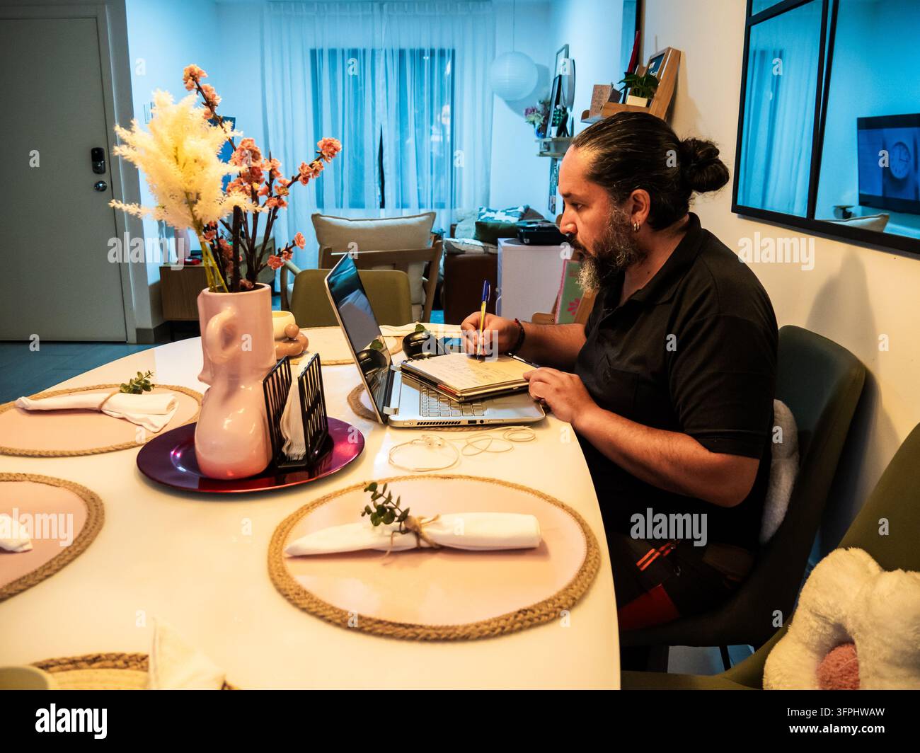 Comp Tabel Person writing notes in a notebook while working on a laptop at a ...