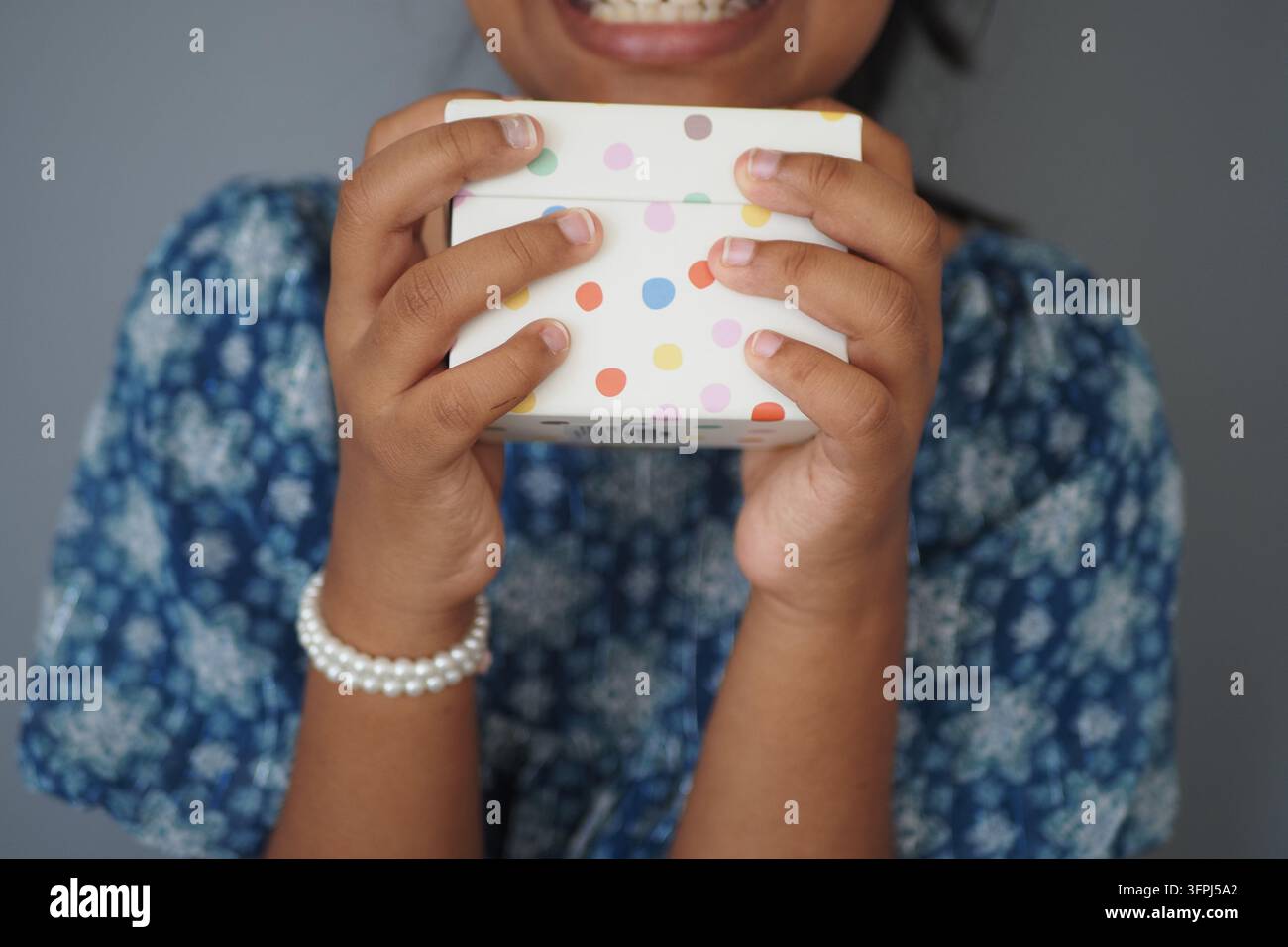 A child smiles while holding a box with colorful dots in her hands ...