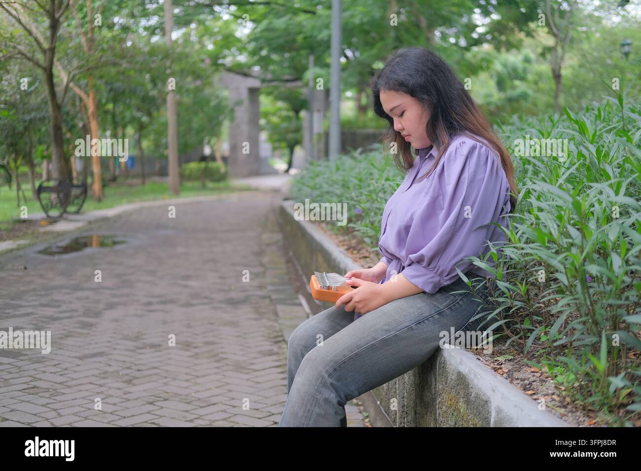 Asian Kitchen Asian woman relaxes in a city park on a sunny summer day, playing a ...