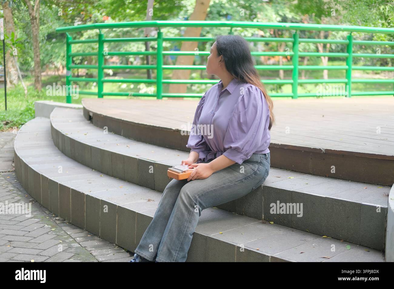 Asian Kitchen Asian woman relaxes in a city park on a sunny summer day, playing a ...