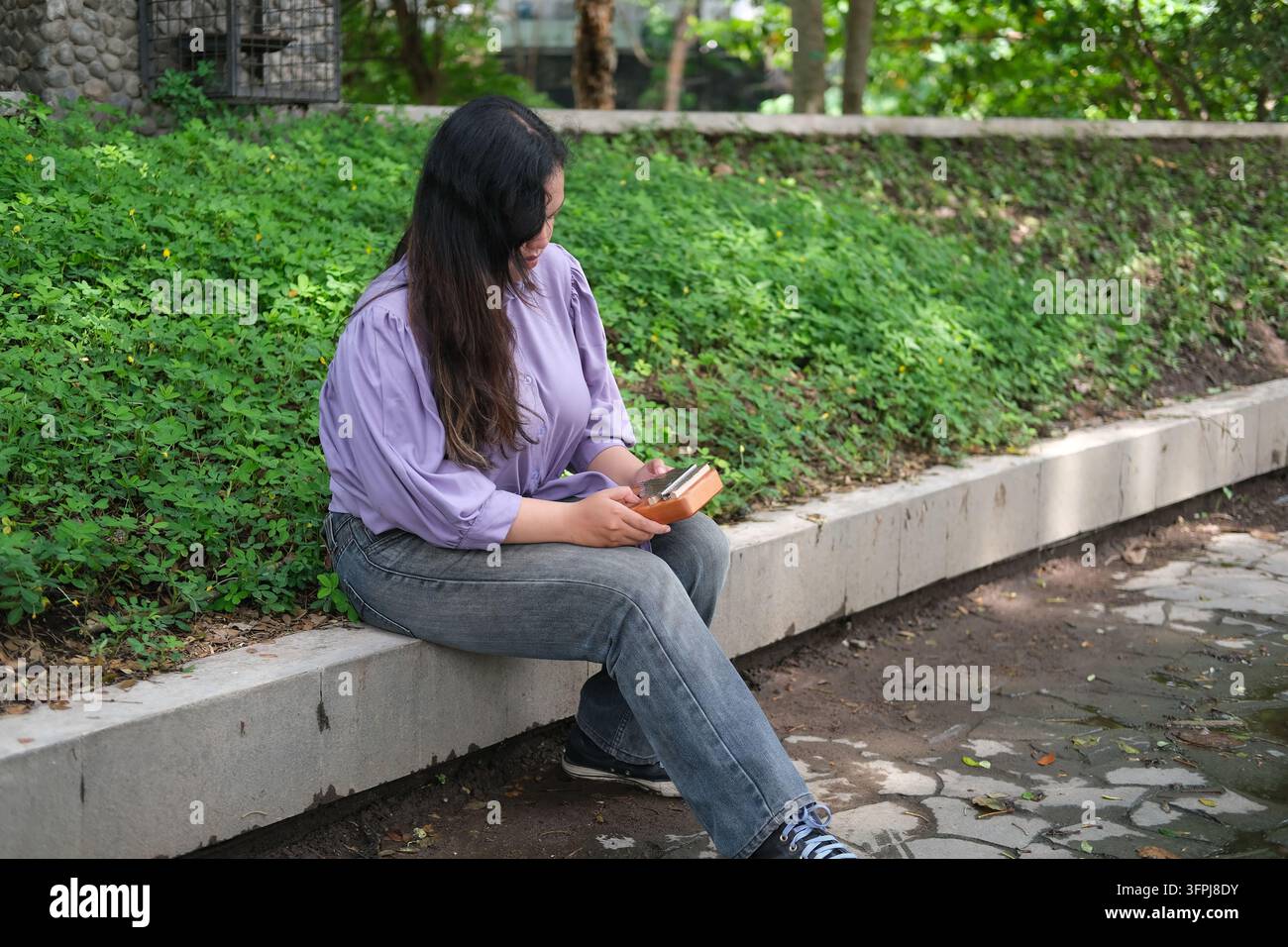 Asian Kitchen young Asian woman plays a kalimba while relaxing in a green city park ...