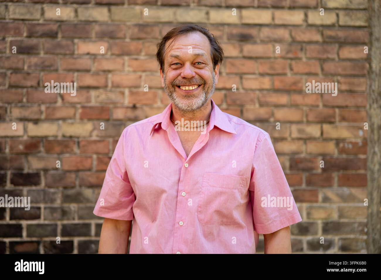 A smiling middle aged man stands in front of a brick wall. Stock Photo