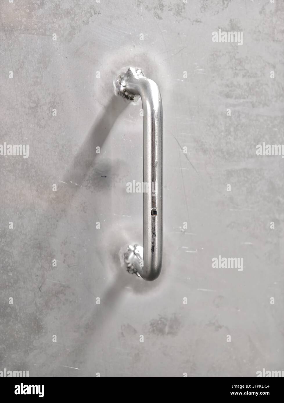 Close-up view shows sleek metallic door handle fixed on brushed steel. Vertical pull bar with rounded ends and smooth reflective finish, with soft sha Stock Photo