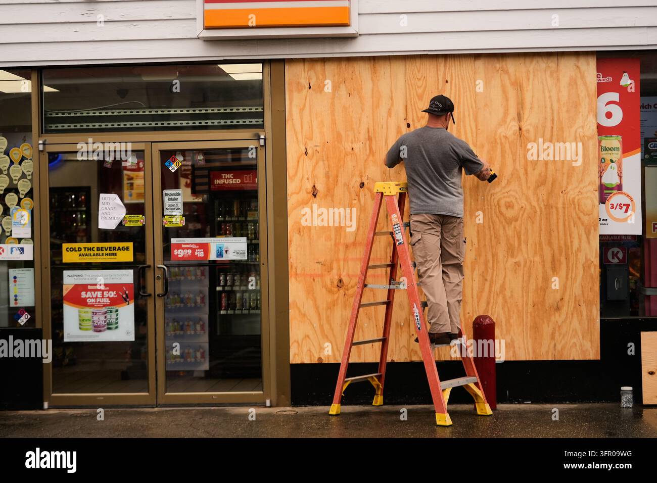 Jason Coffey boards up a convenience store at a gas station as ...