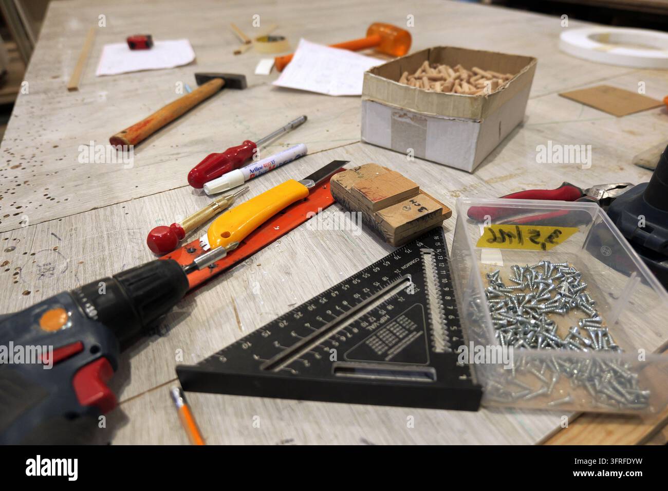 Woodworking tools and carpentry supplies  drill, screws, dowels, speed square and utility knife  arranged on a dusty workbench suggesting an ongoing d Stock Photo