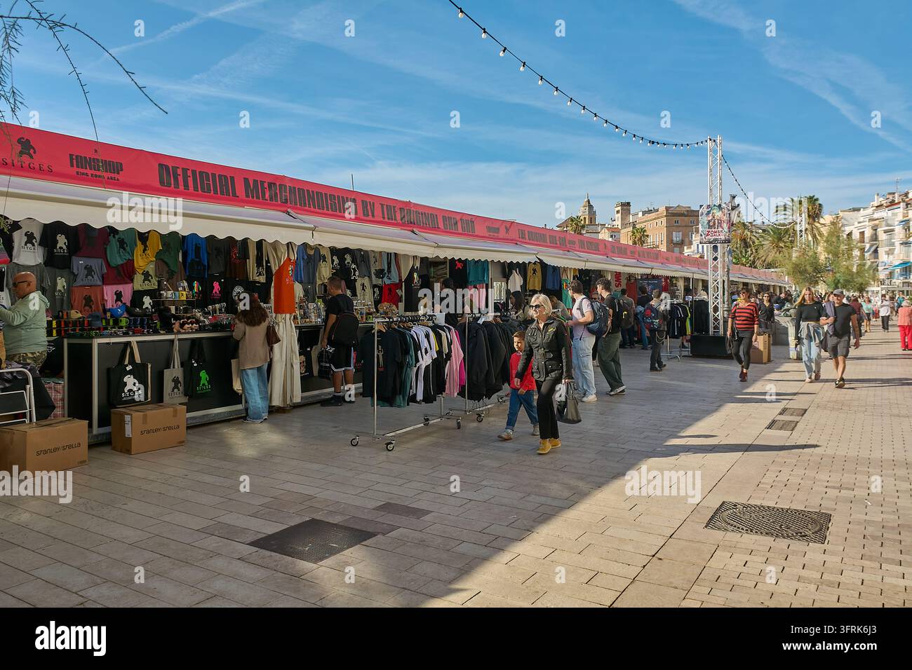 Sitges, Spain - October 10, 2026: People walk past event merchandise ...