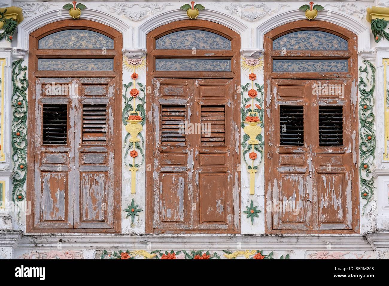 Three weathered wooden shuttered windows with peeling paint, floral ...