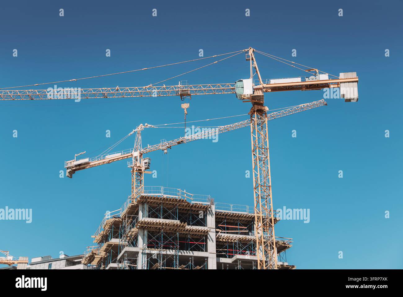 Tower cranes constructing a new residential building, symbolizing growth, development, and progress in an urban landscape Stock Photo