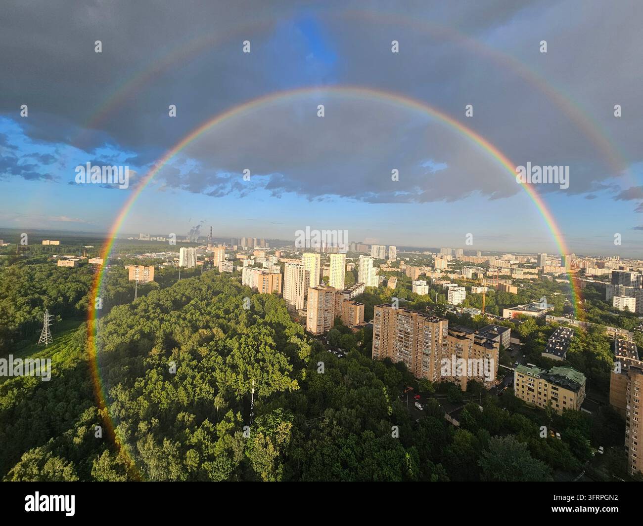Rainbow is seen in the sky above a city. The rainbow is very large and spans the entire sky Stock Photo
