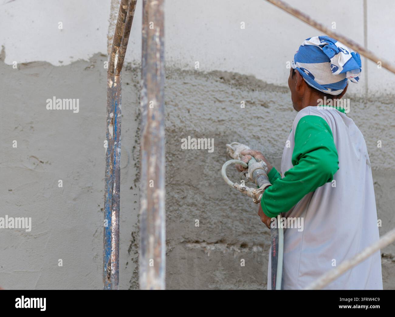 Builder standing on scaffolding while spraying wet concrete plaster on an exterior wall during renovation work. Stock Photo
