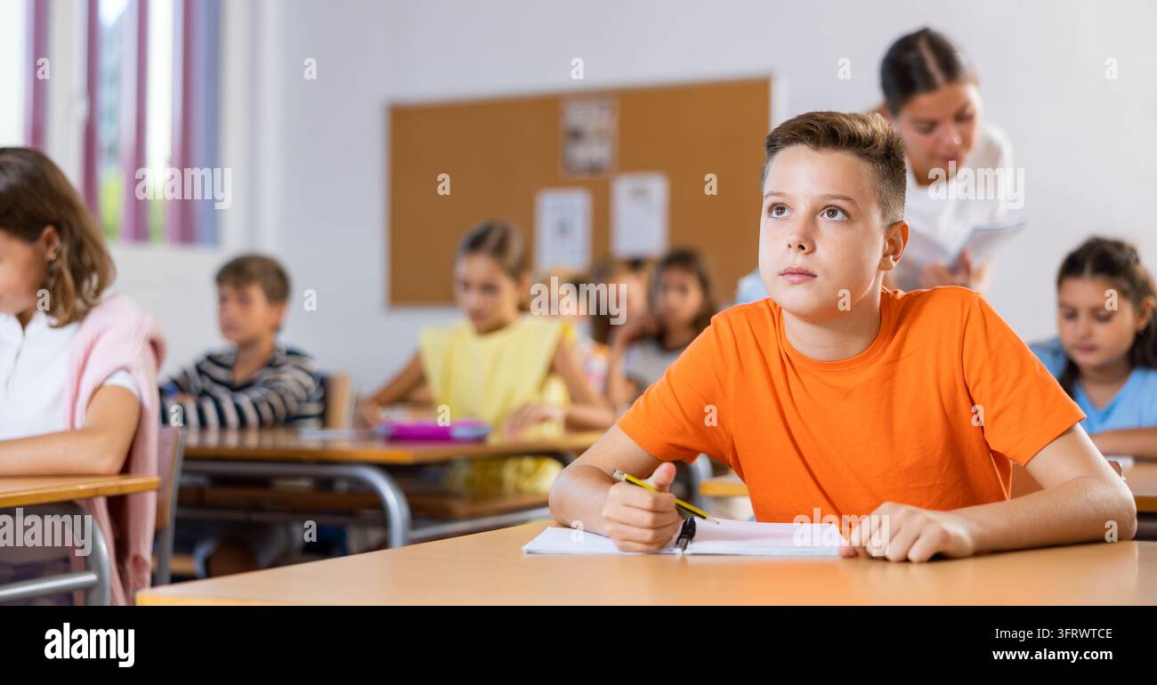 4mb Test Image Young boy sitting at desk in classroom with group of kids and writing ...