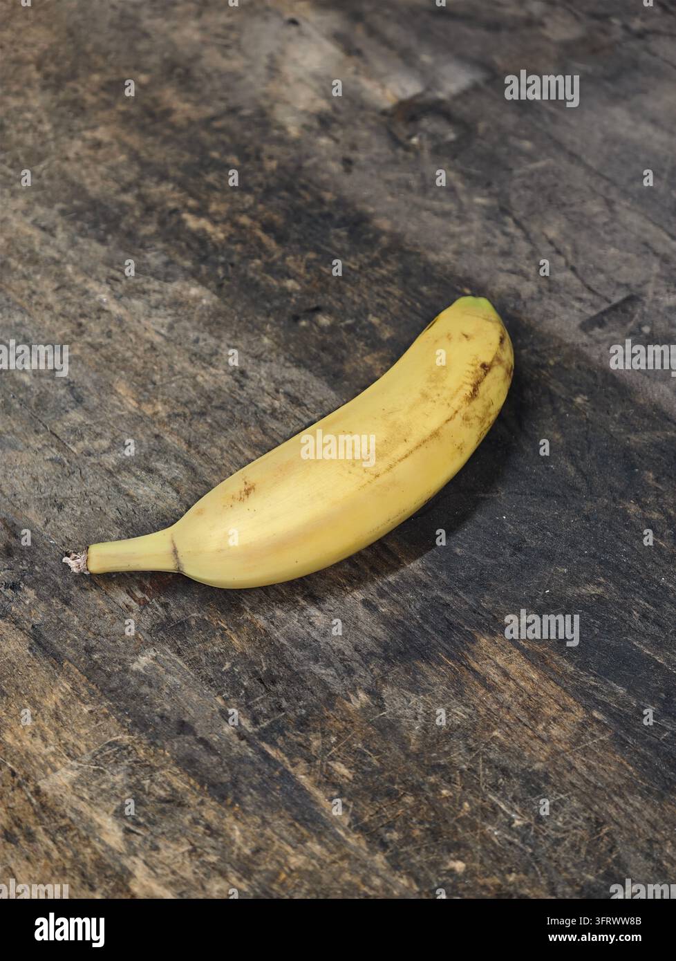Ripe yellow banana with slight brown spots resting on weathered dark ...