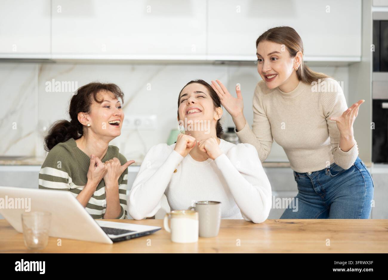 Female friends are sitting at table, reading letter on computer about ...