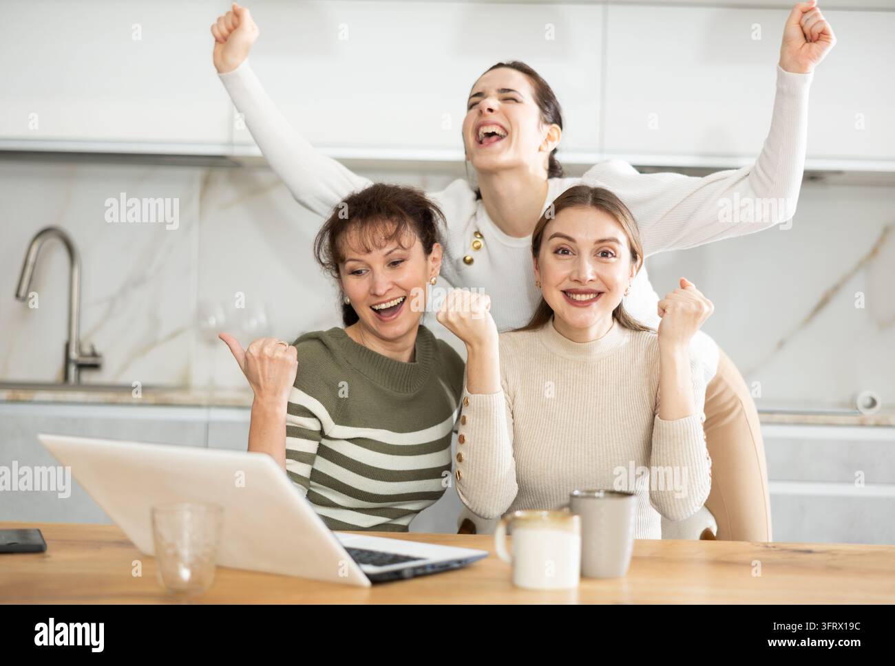 Female friends are sitting at table, reading letter on computer about ...