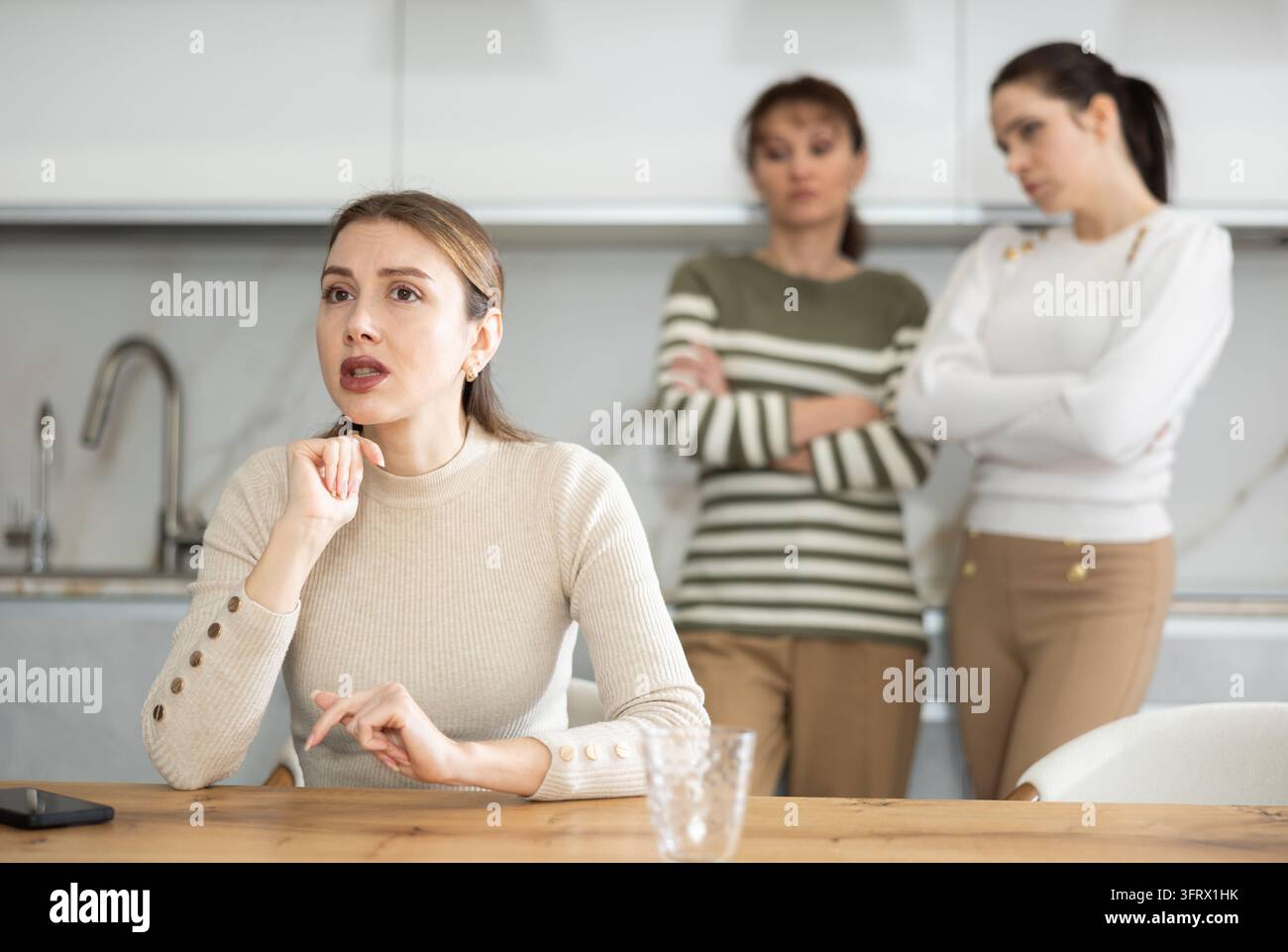 Sad middle-aged woman sitting at table and other women brawling to her ...