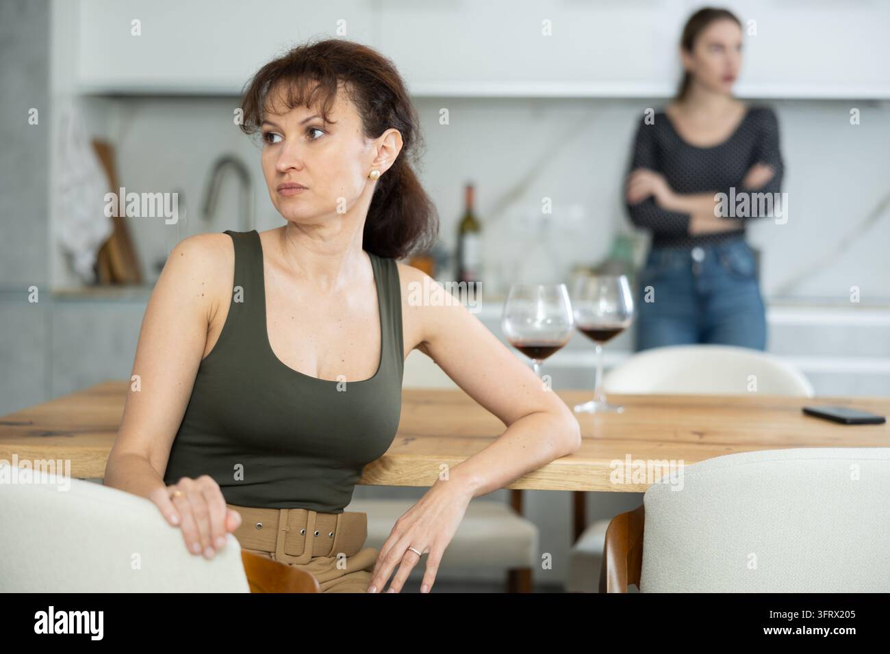 Upset middle-aged woman sitting at the kitchen table with her back to ...
