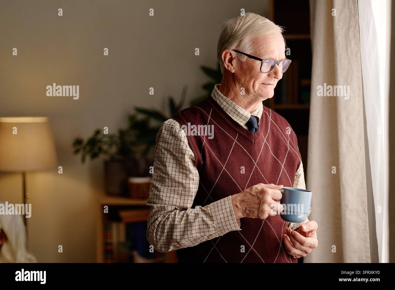 Senior Man Holding Cup Looking through Window at Home Stock Photo