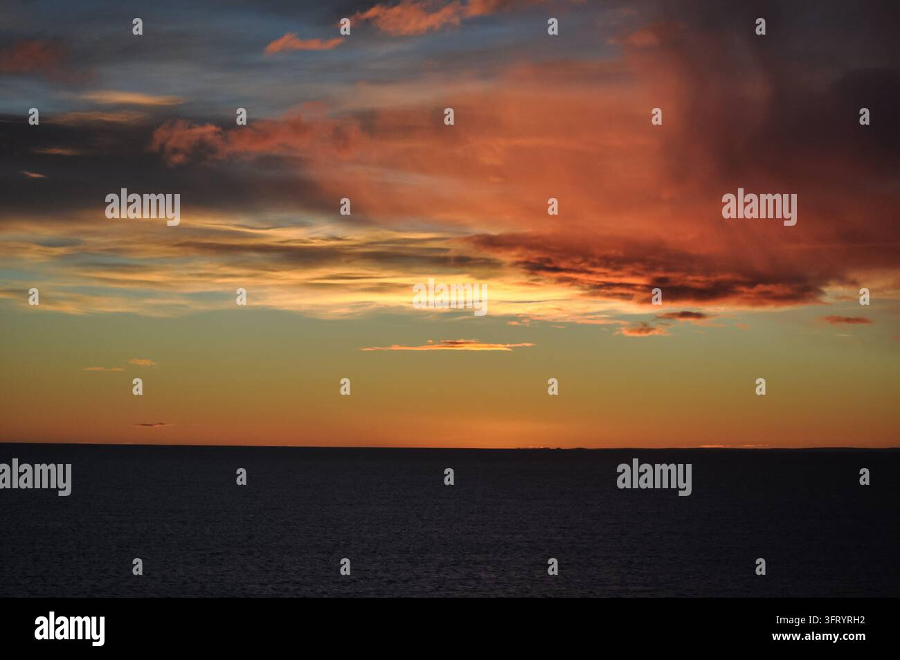 Fiery Red and Orange Sunset Clouds Over the Dark Ocean Horizon Stock Photo
