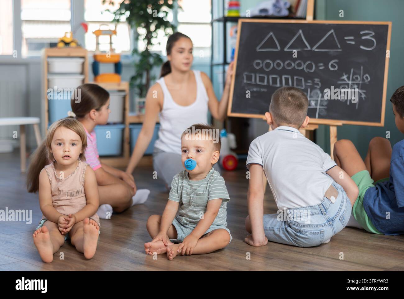 Children sitting on floor in front of blackboard, elementary arithmetic ...