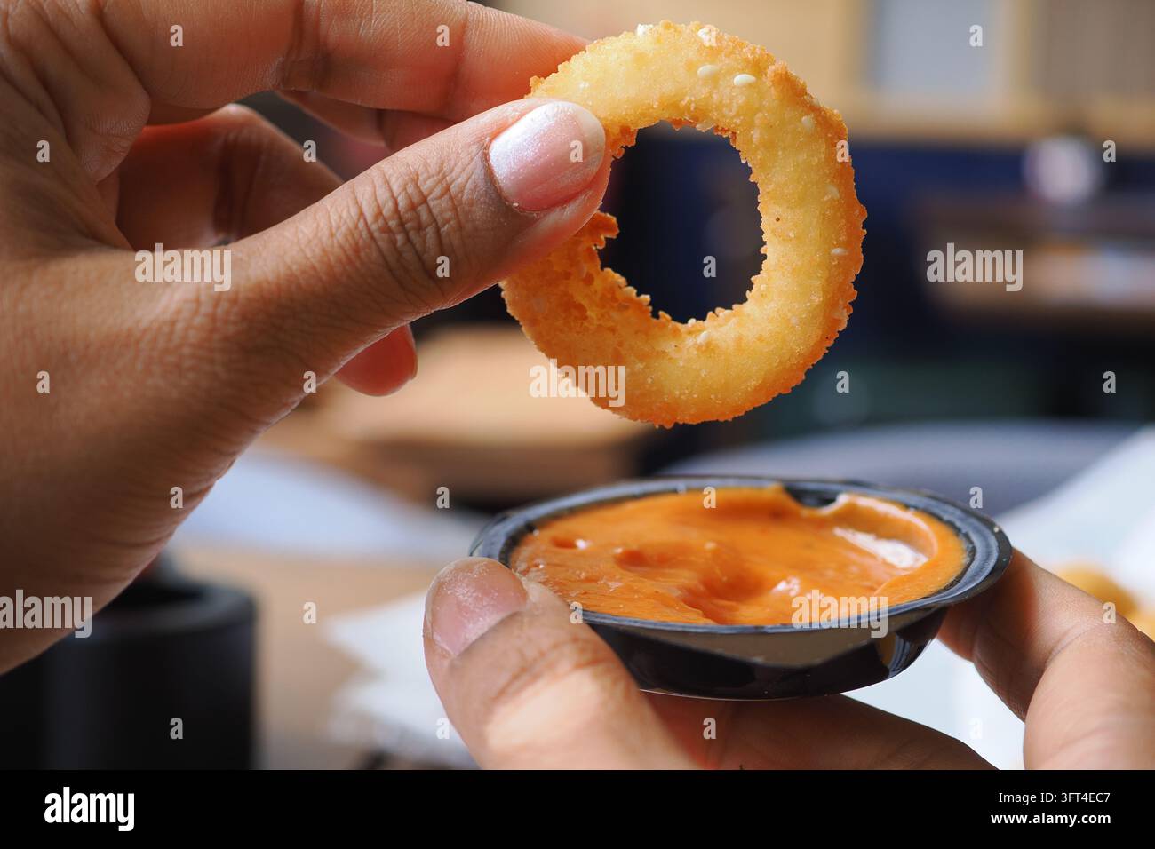 Small Inion Hand holding a fried onion ring above a small container of dipping ...