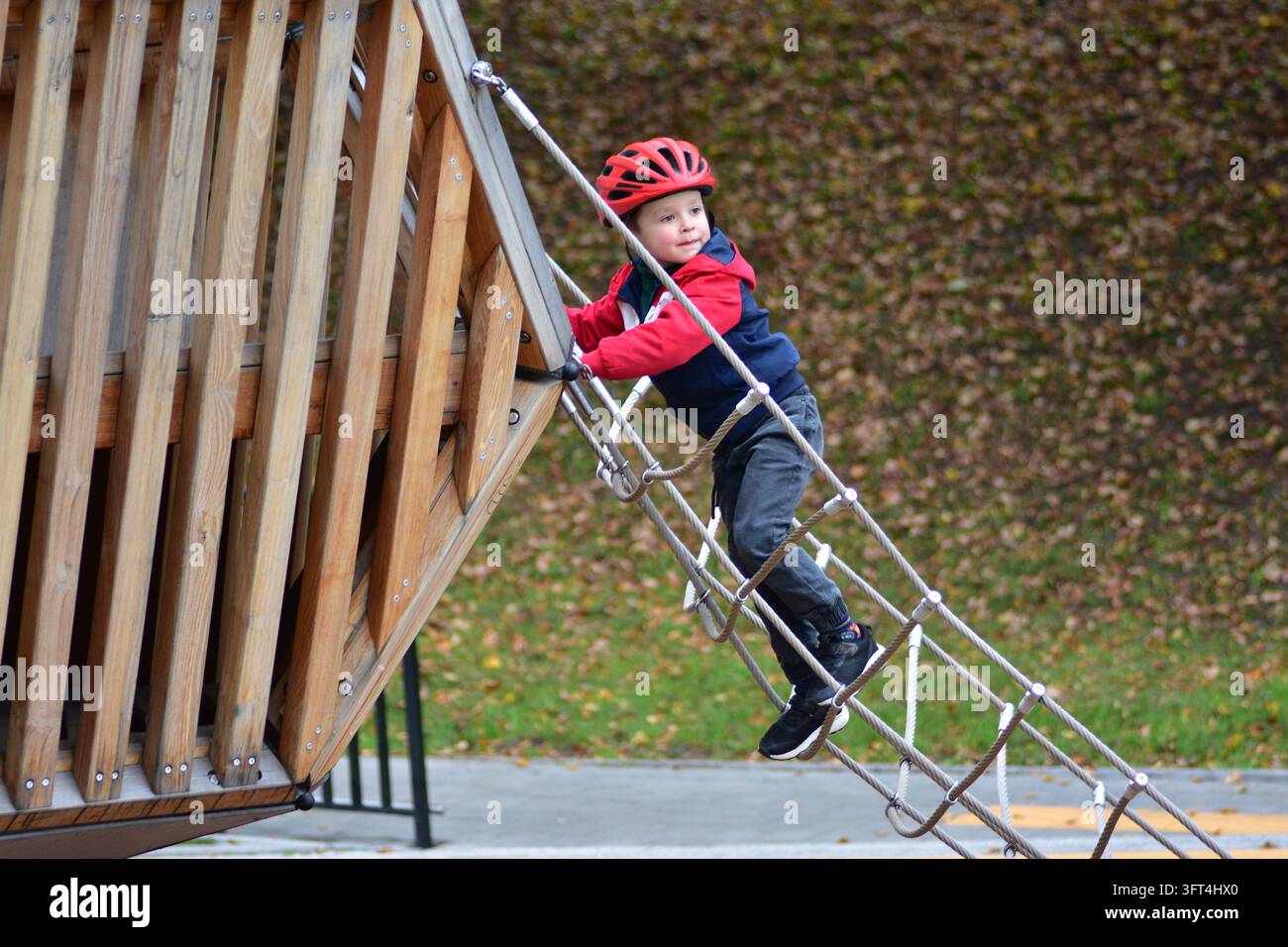 Young boy wearing a red safety helmet climbing a rope bridge on a ...