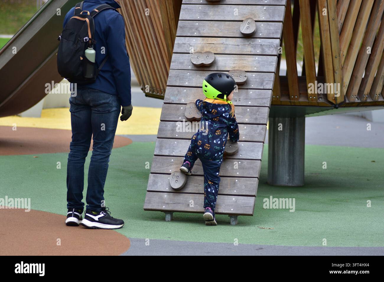 Young girl wearing a safety helmet climbing a wooden playground wall ...