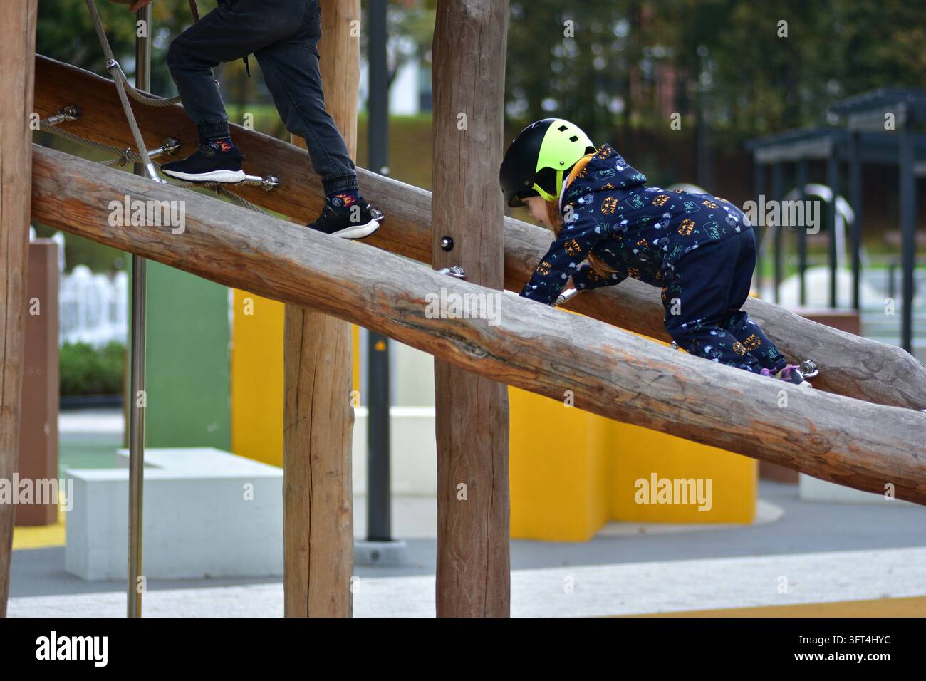 Young girl wearing a safety helmet climbing a wooden playground ...