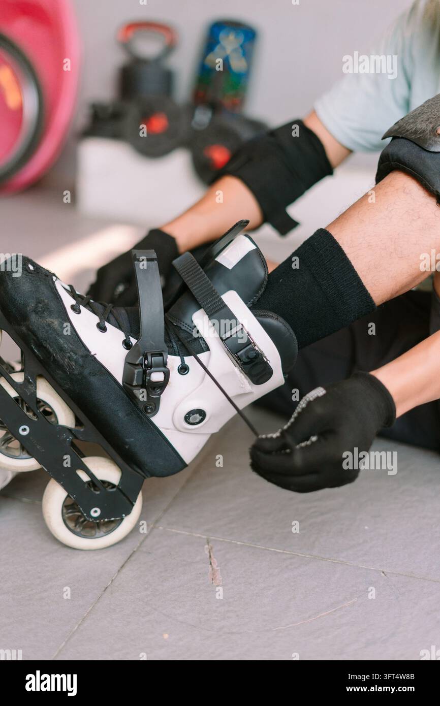 A person sitting on the ground fastens and ties inline skates while ...