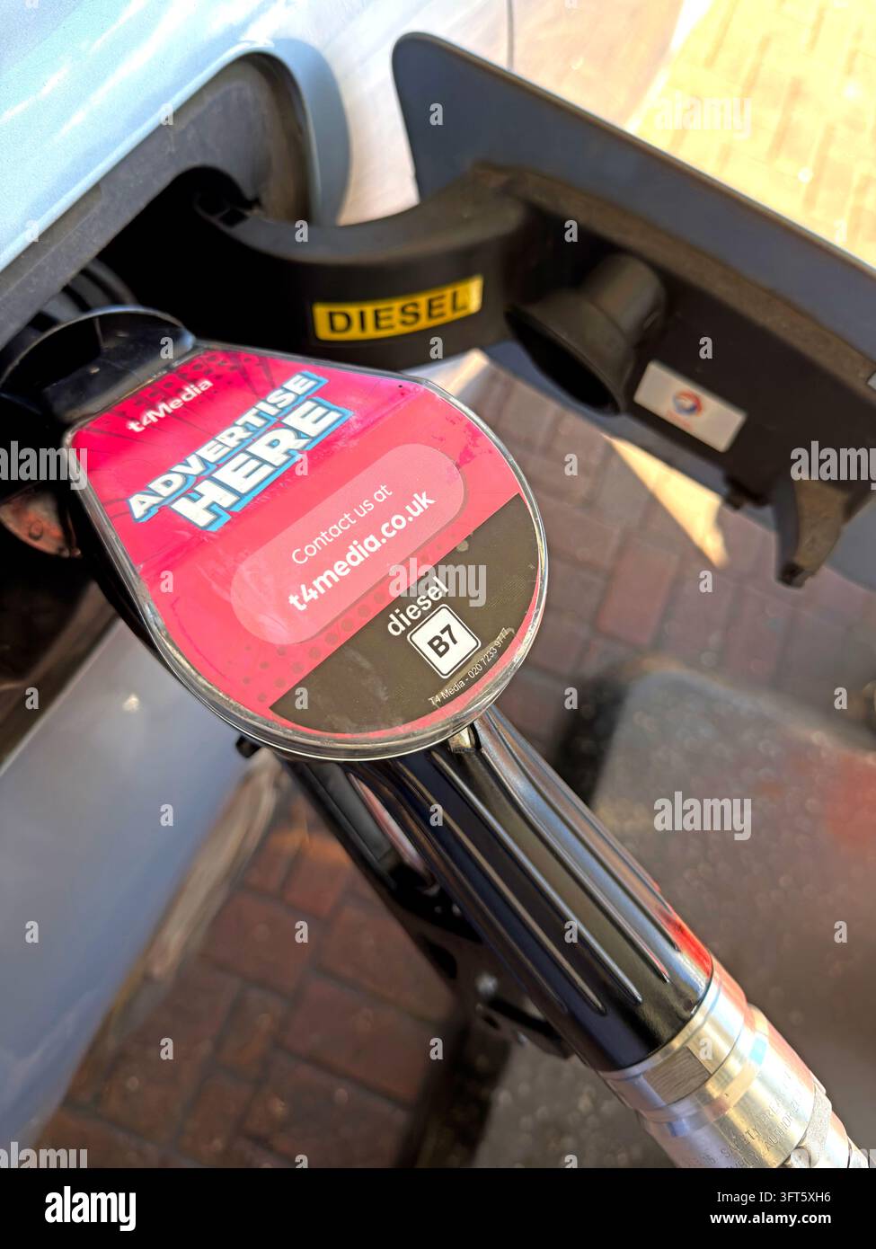Motorist refuelling a diesel car, with the pump nozzle and fuel grade visible at the filler opening. Stock Photo