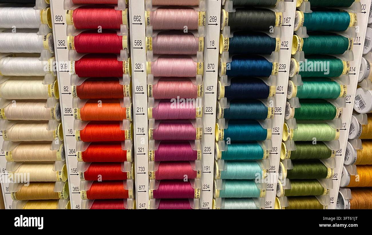 Assorted colorful sewing thread spools in different shades arranged on display racks at craft supply store Stock Photo