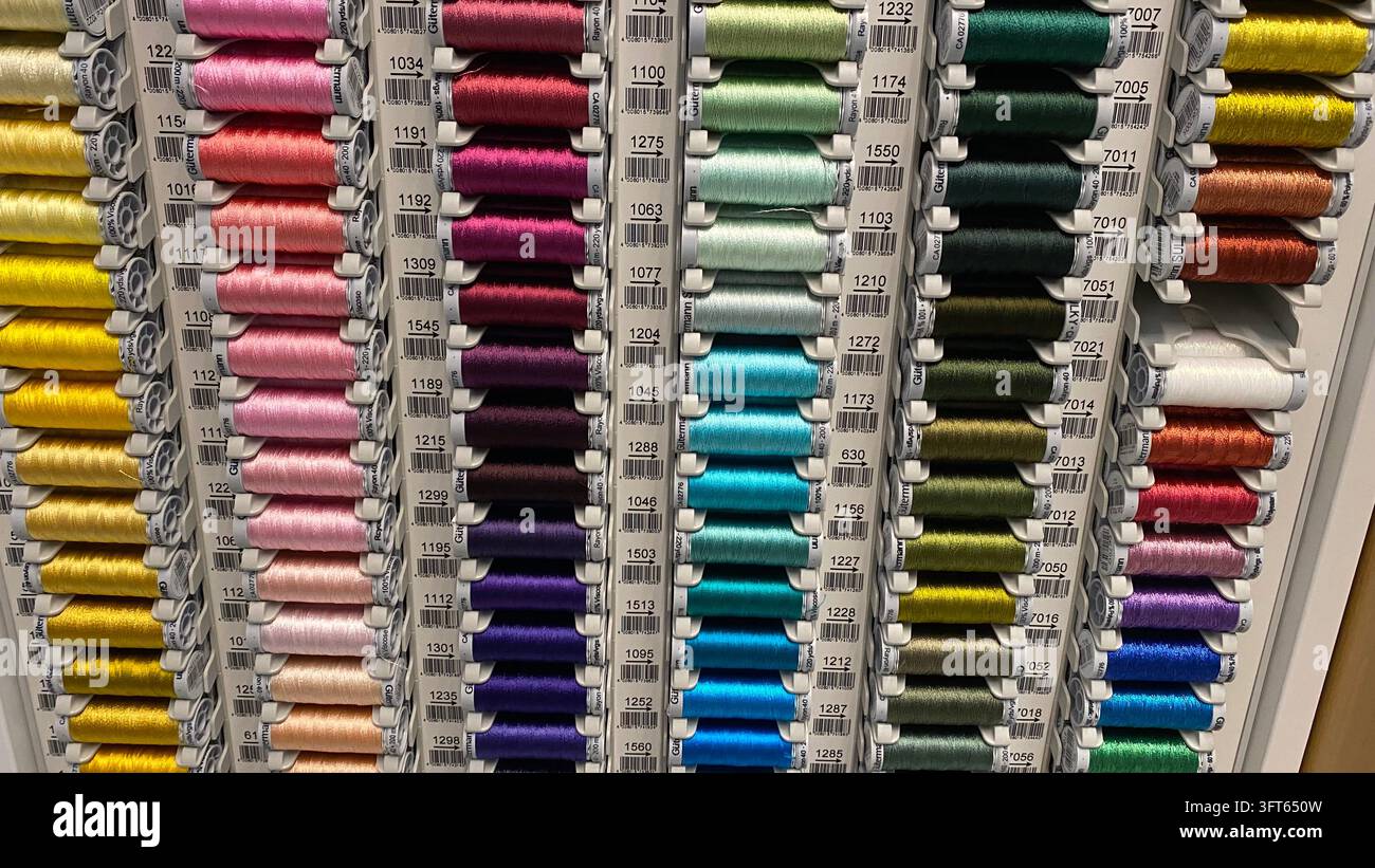 Assorted colorful sewing thread spools in different shades arranged on display racks at craft supply store Stock Photo