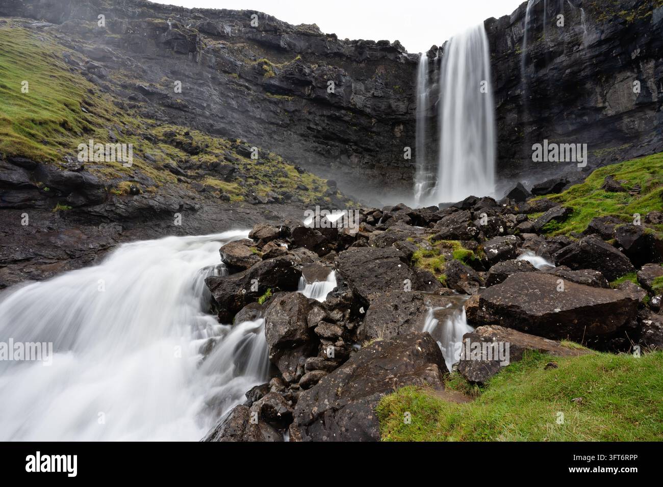 View of a powerful waterfall cascading over dark volcanic cliffs into a ...