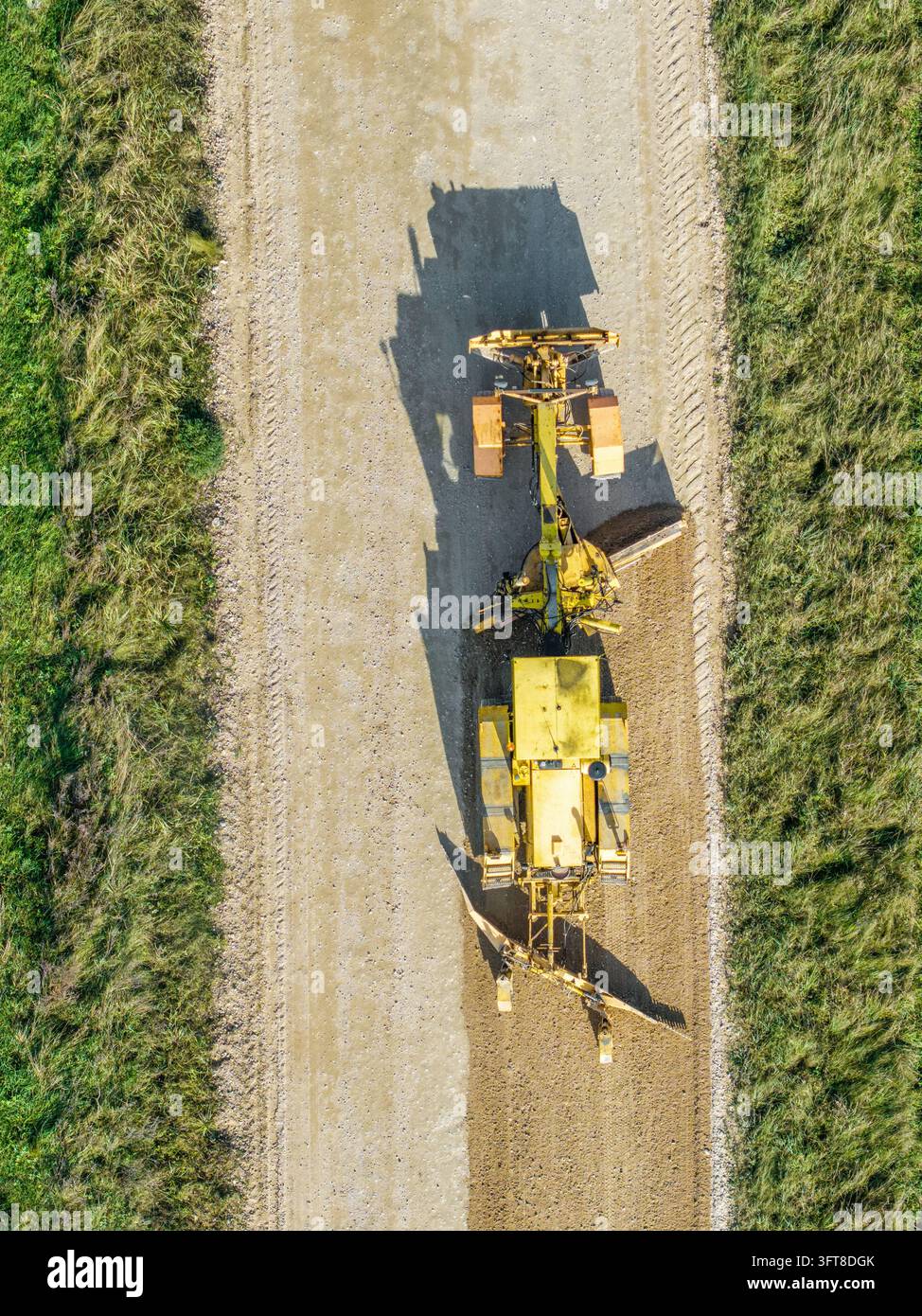 Aerial view of a yellow motor grader leveling and reshaping the surface ...