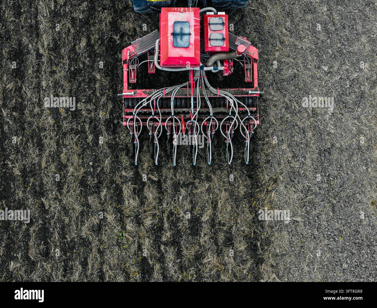 Aerial view of a red agricultural seeder machine working on a dark soil ...