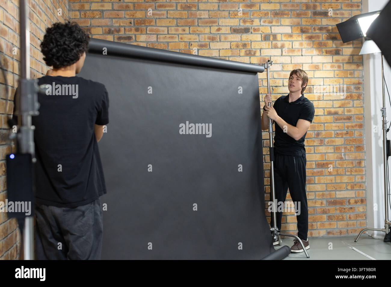 Two men installing large black paper backdrop in studio, holding ...