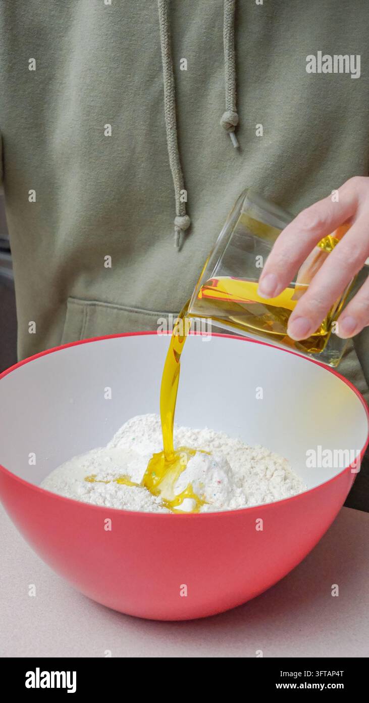 Individual wearing a green hoodie is pouring oil from a glass container ...