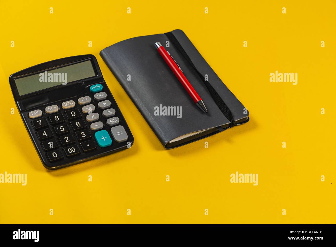 A calculator and notebook with a pen sit on a yellow surface ready for ...