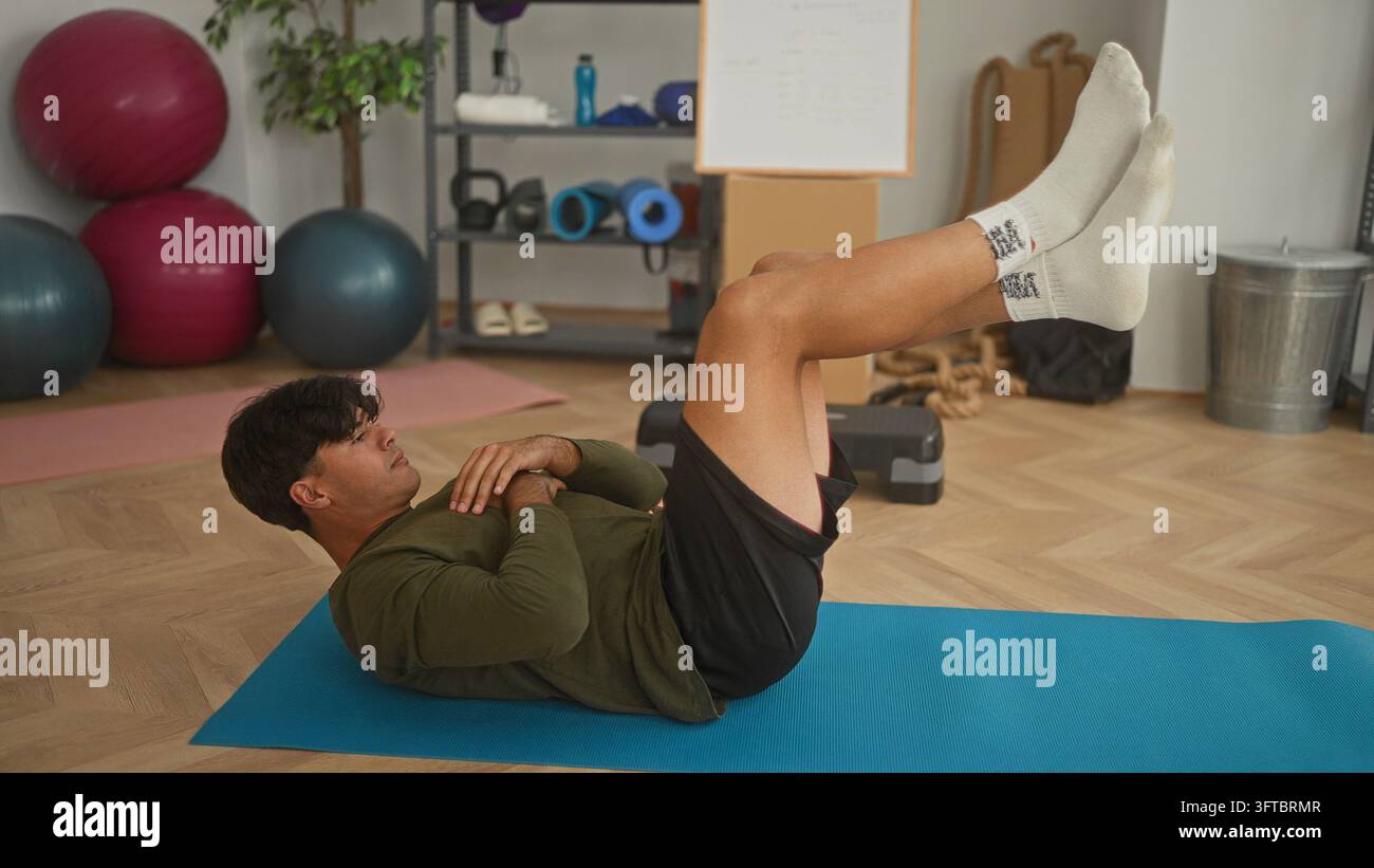 Man lying on mat with legs raised and hands crossed on chest performing abdominal crunch in studio; core strength focus. Stock Photo