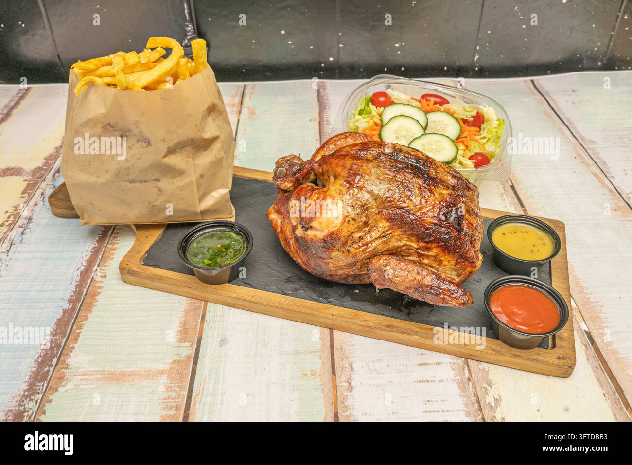 Whole lacquered rotisserie chicken on a slate board with green, mustard ...