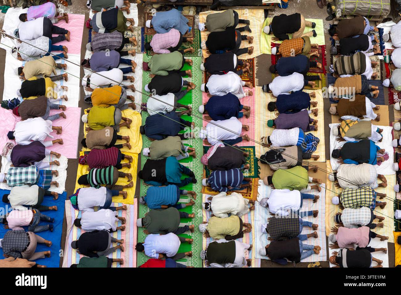Overhead view of worshippers bowing in prostration in neat rows on bright prayer mats spread across a road, West Bengal, Kolkata, India Stock Photo